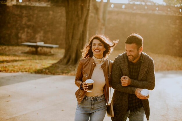 Przystojna młoda para spacerująca w jesiennym parku z kawą na wynos w rękach