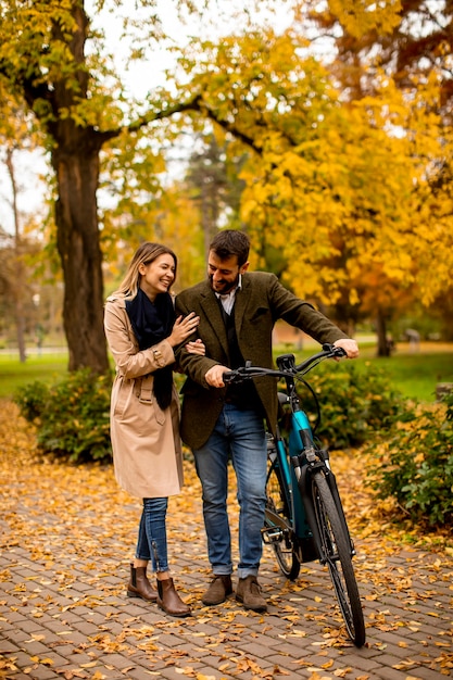 Przystojna młoda para w jesiennym parku z elektrycznym rowerem
