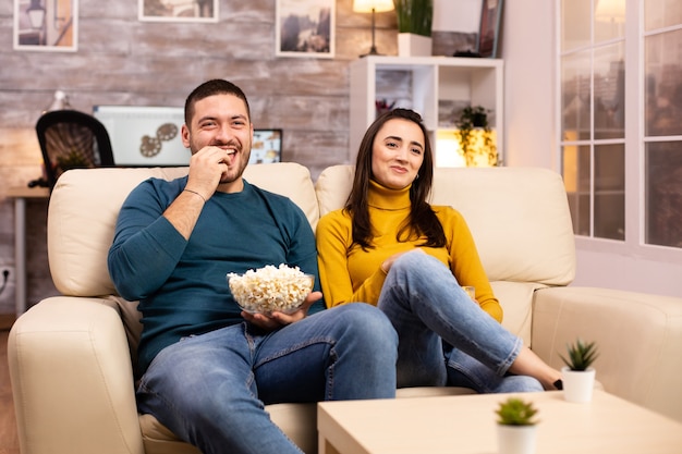 Przystojna Para W Domu Jedząca Popcorn I Oglądając Telewizję Na Kanapie W Salonie