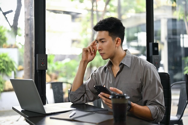 Przystojny azjatycki biznesmen koncentruje się na swojej pracy biznesowej przy użyciu laptopa w kawiarni