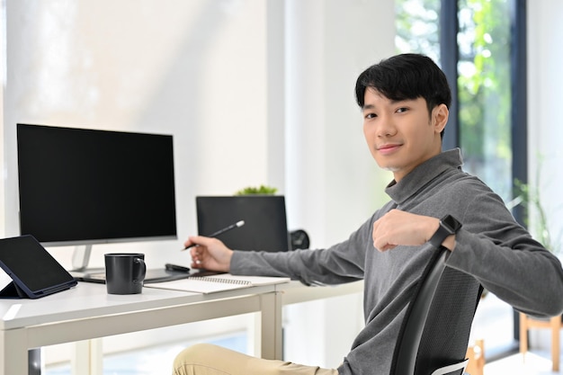 Przystojny azjatycki grafik lub programista siedzi przy biurku w nowoczesnym biurze