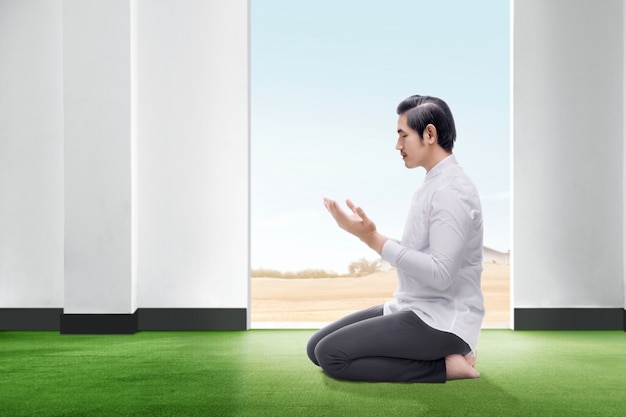 Przystojny Azjatycki Mężczyzna Siedzący W Pozycji Modlitwy Zamyka Oczy I Unosi Ręce Na Dywanie W Pokoju