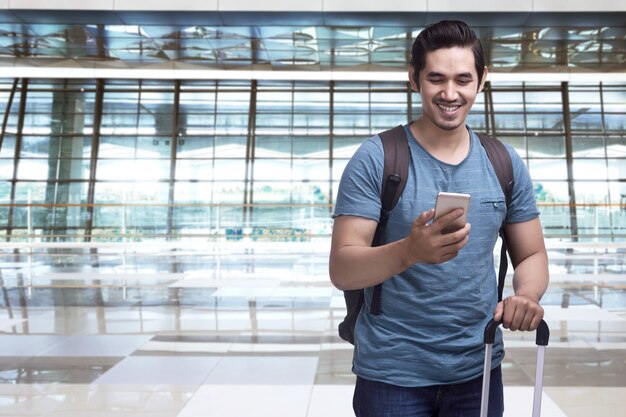 Przystojny azjatykci mężczyzna podróżnik z walizki mienia smartphone