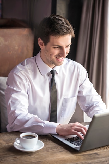 Przystojny biznesmen pracuje przy laptopem z filiżanką kawy.