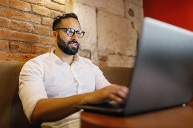 Przystojny biznesmen w zwykłych ubraniach używa laptopa i uśmiecha się podczas pracy w restauracji