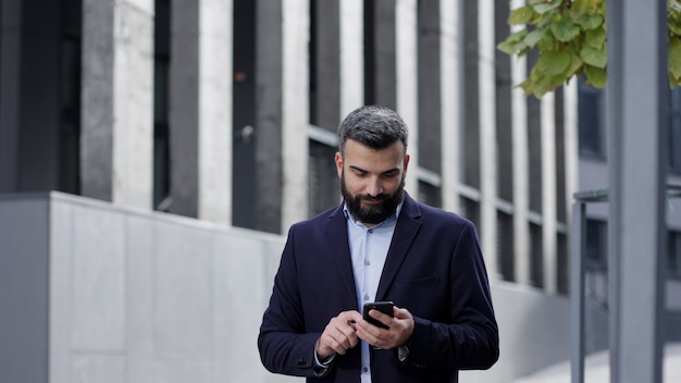 Przystojny biznesmen za pomocą smartfona stojącego w pobliżu centrum biznesowego.