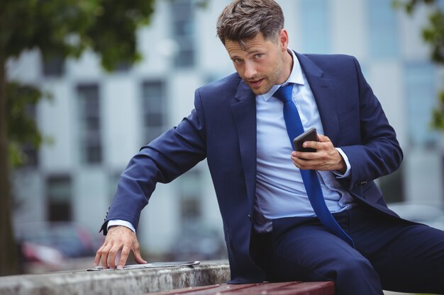 Przystojny biznesmena mienia telefon komórkowy podczas gdy używać cyfrową pastylkę