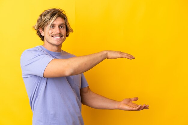 Przystojny blondyn na białym tle na żółty trzymając copyspace, aby wstawić reklamę