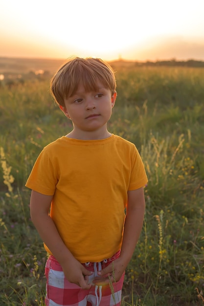 przystojny blondyn w żółtej koszulce stoi na polu w promieniach zachodzącego słońca