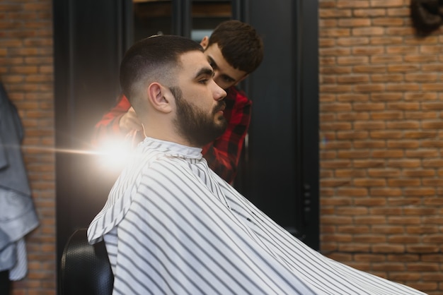 Przystojny brodaty mężczyzna uśmiecha się podczas obcinania włosów przez fryzjera w salonie fryzjerskim