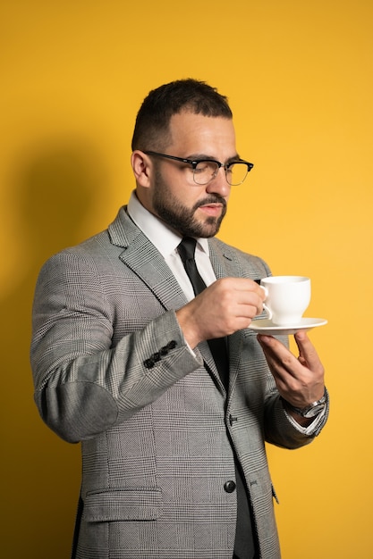 Przystojny Brodaty Mężczyzna W Okularach W Wizytowym, Trzymając Filiżankę Kawy Na żółtym Tle