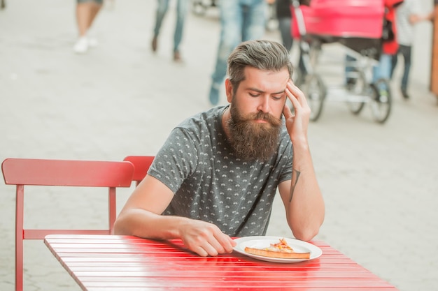 Przystojny brodaty mężczyzna z pizzą w kawiarni