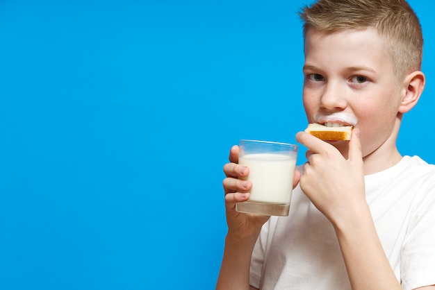 Przystojny chłopak z białym wąsem od picia mleka i jedzenia kawałka chleba.