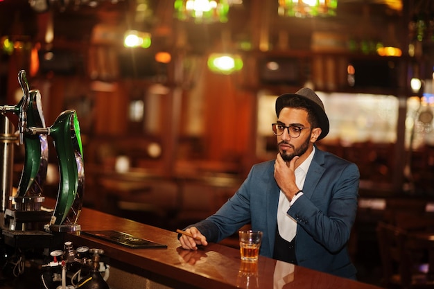 Przystojny, dobrze ubrany arab ze szklanką whisky i cygarem pozował w pubie