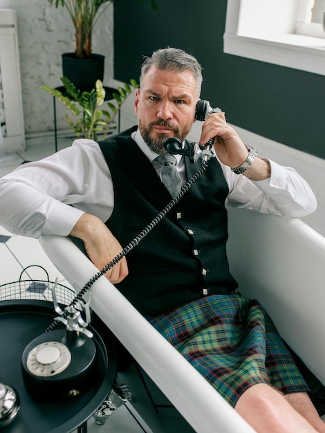 przystojny dojrzały odważny stylowy mężczyzna Szkot w kilcie i garniturze rozmawia przez telefon z domu