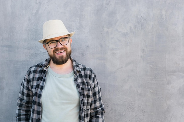 Przystojny facet turysta wyglądający szczęśliwy noszący słomkowy kapelusz do podróżowania stojący na tle betonowej ściany z kopią przestrzeni