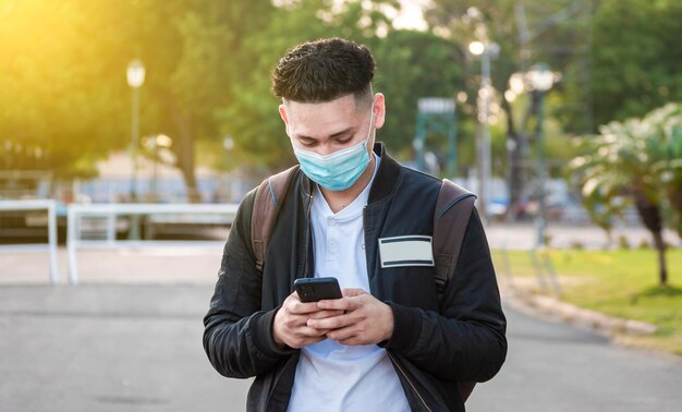 Przystojny facet wysyła SMS-y swoim telefonem Przystojny młody mężczyzna w masce na twarz wysyła SMS-y swoim telefonem Przystojny mężczyzna pisze SMS-y na swoim telefonie
