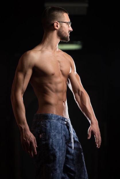 Zdjęcie przystojny geek mężczyzna stojący silny na siłowni i napinający mięśnie mięśni atletyczny kulturysta model fitness pozujący po ćwiczeniach