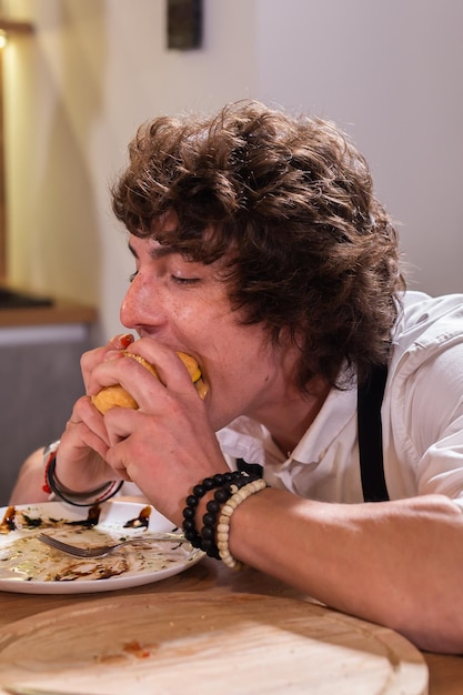 Przystojny głodny mężczyzna cieszący się pysznym burgerem fastfood i niezdrową koncepcją jedzenia