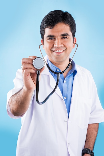 Przystojny indyjski mężczyzna lekarz bada stetoskopem w powietrzu. stojąc na białym tle na niebieskim tle