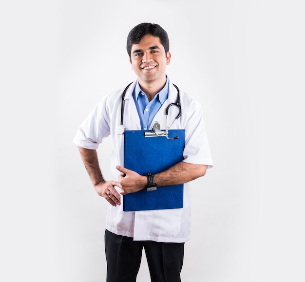 Przystojny indyjski mężczyzna lekarz z podkładką do pisania lub kartą medyczną lub raportem, stojący na białym tle nad białym tłem