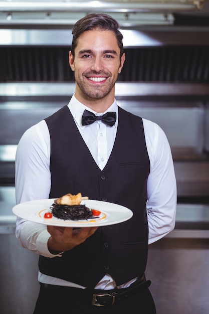 Przystojny kelner trzyma talerz spaghetti atramentu kałamarnicy