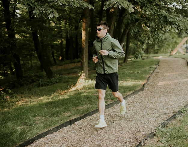 Przystojny lekkoatletyczny młody mężczyzna biega podczas treningu w słonecznym zielonym parku
