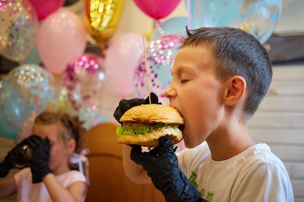 Przystojny mały chłopiec je burgera w czarnych gumowych rękawiczkach