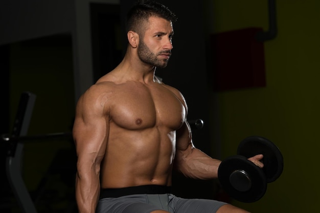 Przystojny mężczyzna ćwiczący bicepsy w ciemnych lokach z hantlami na siłowni
