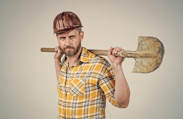 Przystojny mężczyzna ekspert w dziedzinie budowy kasku ochronnego i koszuli w kratkę na placu budowy z zajęciem łopaty