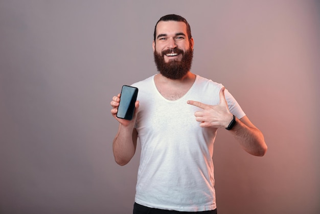 Przystojny mężczyzna hipster wskazuje na pusty ekran telefonu, który trzyma