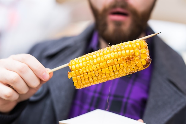 Zdjęcie przystojny mężczyzna je pyszne kolby kukurydzy na ulicy.