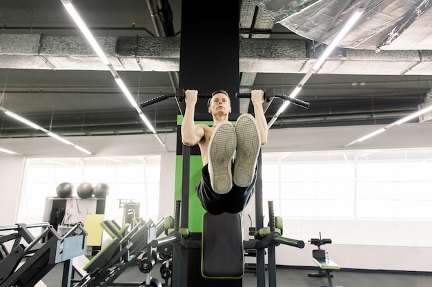 Przystojny mężczyzna półnagi robi pull-up w pozycji L-sit na poziomym pasku na siłowni. Trening kalisteniczny.