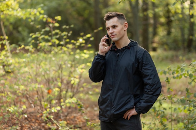 Przystojny mężczyzna rozmawia przez telefon w jesiennym lesie