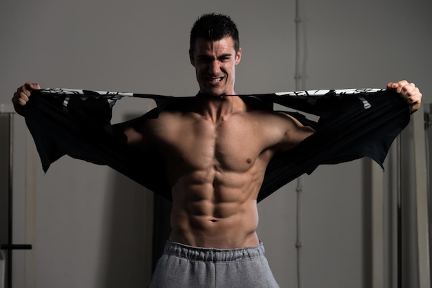 Przystojny mężczyzna stojący mocno na siłowni i zrywający koszulkę muskularny atletyczny kulturysta Model fitness pozuje po ćwiczeniach