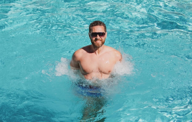 Przystojny mężczyzna w okularach przeciwsłonecznych pływających w basenie letnim wakacjach