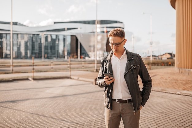 Przystojny Mężczyzna W Okularach Ze Smartfonem Na Ulicy Wielkiego Miasta. Biznesmen Rozmawia Przez Telefon Na Tle Miejskim