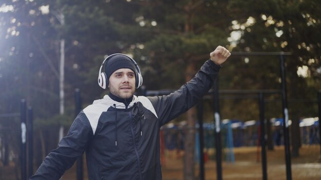Przystojny mężczyzna w słuchawkach robi ćwiczenia rozciągające podczas słuchania muzyki w parku zimowym