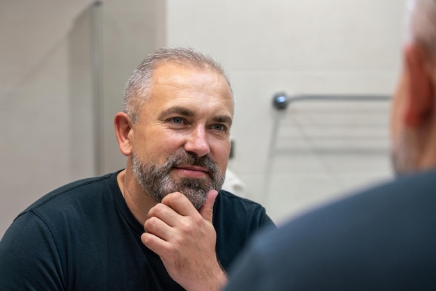Przystojny mężczyzna w średnim wieku patrzący w lustro w łazience