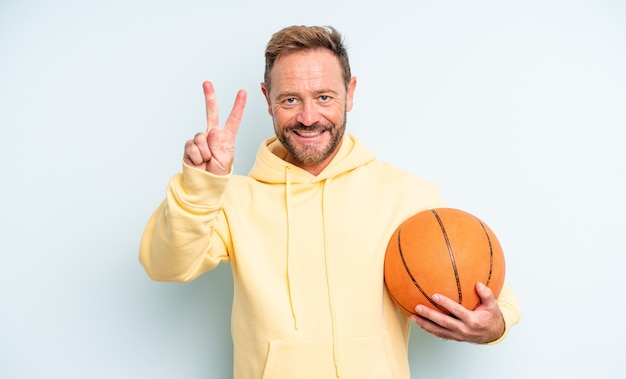 Przystojny mężczyzna w średnim wieku, uśmiechnięty i przyjazny, pokazując numer dwa. koncepcja koszykówki