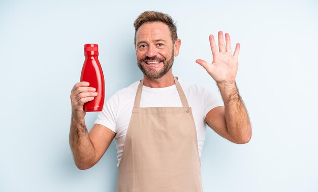 Przystojny mężczyzna w średnim wieku, uśmiechnięty i przyjazny, pokazując numer pięć. koncepcja ketchupu