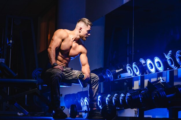 Przystojny mężczyzna z dużymi mięśniami pozuje do kamery na siłowni Czarno-niebieskie tło Portret kulturysty Zbliżenie