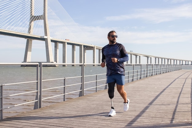 Przystojny mężczyzna z mechaniczną nogą na nasypie. Kaukaski mężczyzna w sportowe ubrania jogging w letni dzień. Koncepcja sportu, rekreacji, niepełnosprawności