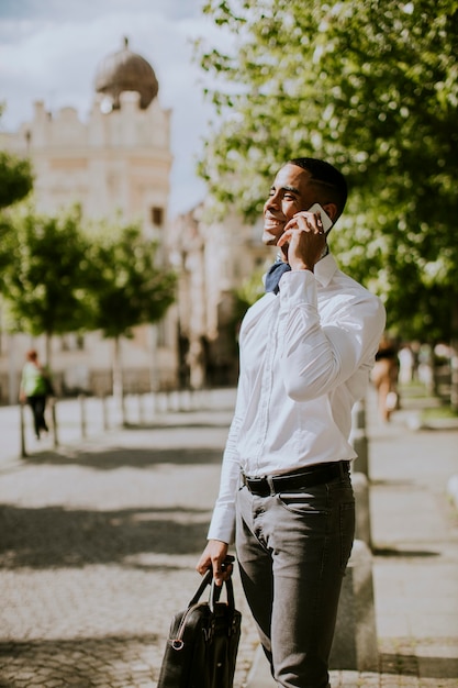 Przystojny młody Afroamerykański biznesmen korzystający z telefonu komórkowego podczas oczekiwania na taksówkę na ulicy