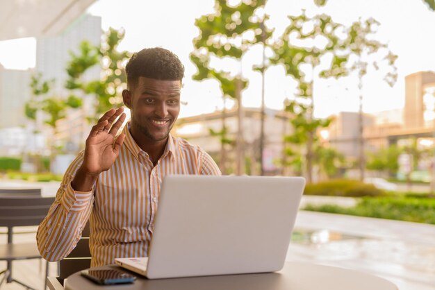 Przystojny Młody Afrykański Biznesmen W Mieście Za Pomocą Laptopa W Kawiarni I Rozmawiając Wideo