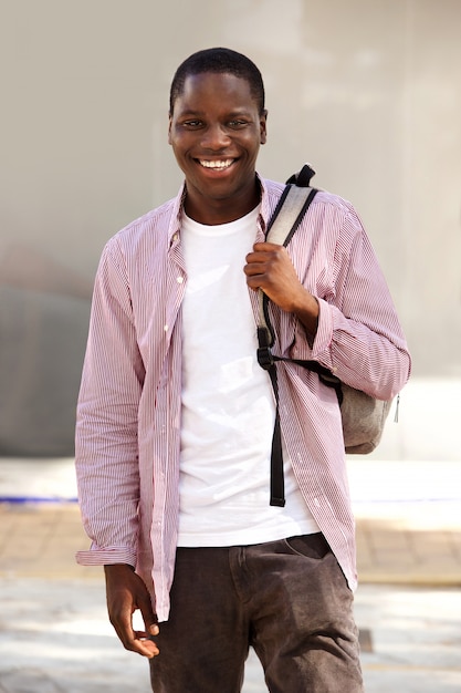 Przystojny młody afrykański uczeń ono uśmiecha się outdoors z torbą