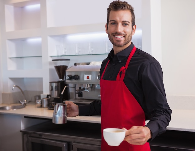 Przystojny młody barista trzyma dzbanek i filiżankę kawy