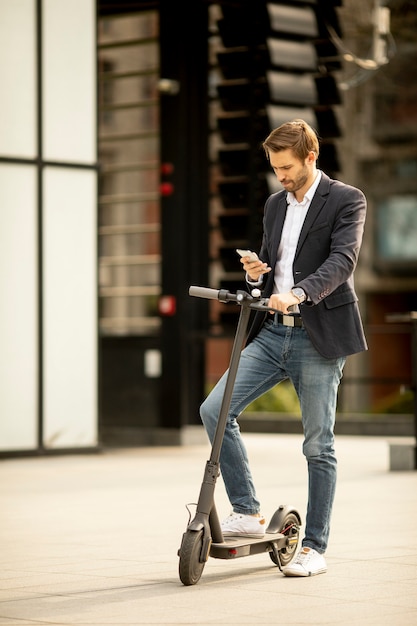 Przystojny młody biznesmen za pomocą telefonu komórkowego na skuter elektryczny