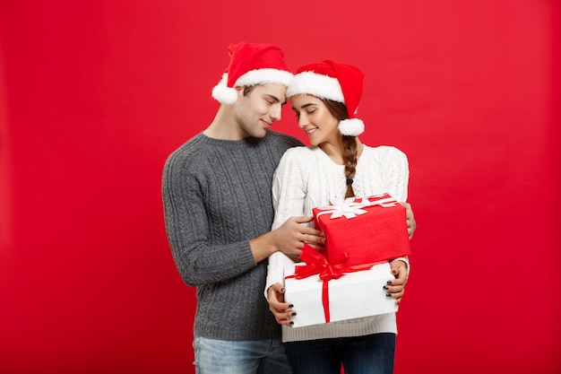 przystojny młody chłopak w świątecznym swetrze zaskoczy swoją dziewczynę prezentami.