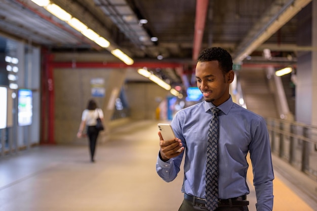 Przystojny młody czarny biznesmen ubrany w koszulę i krawat w poziomym ujęciu peronu stacji